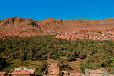 Panoramic view of the majestic Atlas Mountains in Morocco, showcasing a traditional Berber village and lush valleys, ideal for excursions and cultural immersion from Marrakech.